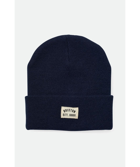 Navy blue beanie with a logo patch on a light gray background
